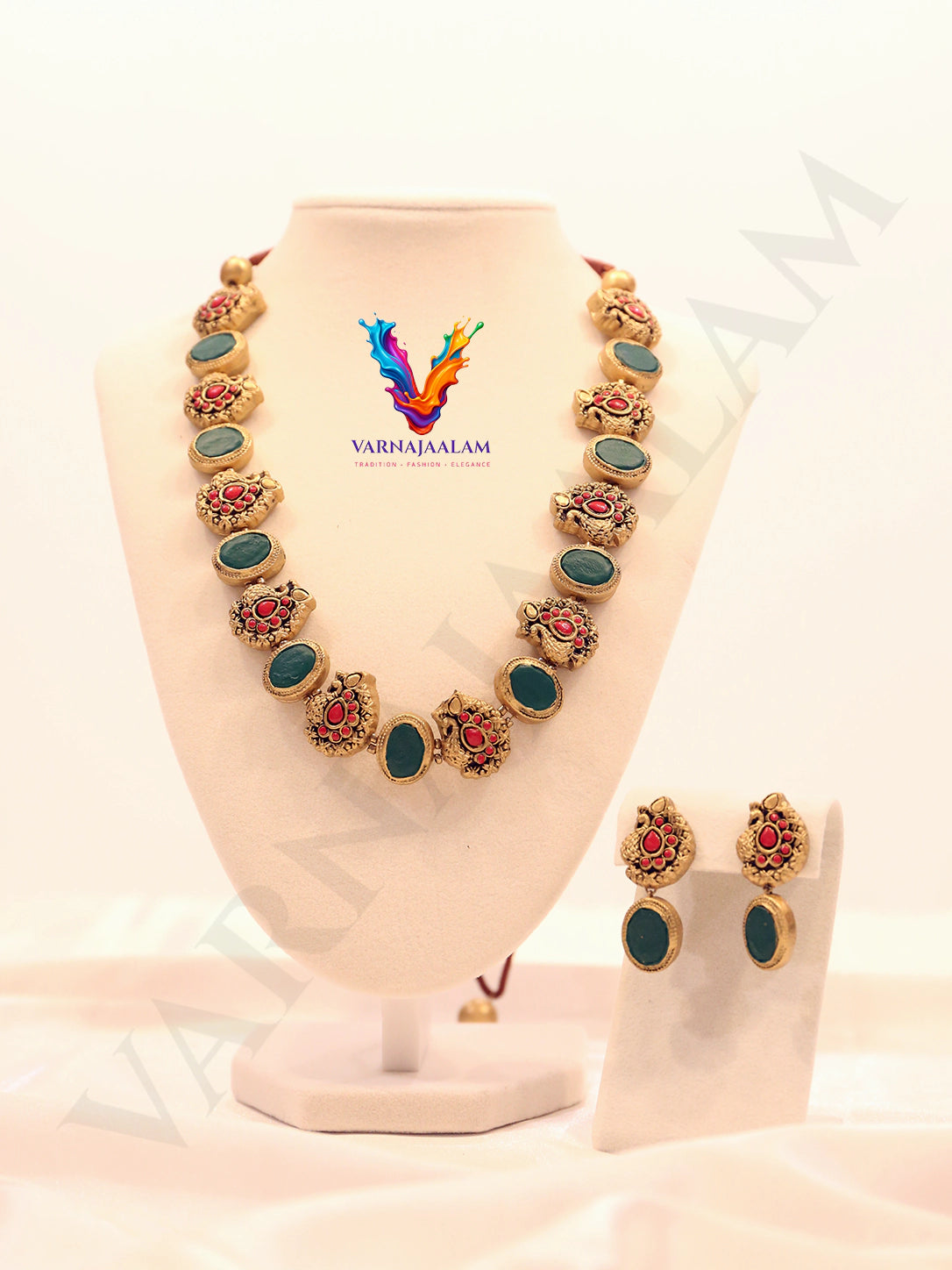 Handcrafted terracotta mala necklace set featuring alternating oval dark green stones and antique gold peacock motifs with red accents, with matching peacock drop earrings