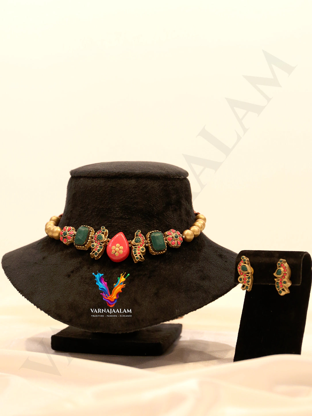 Handcrafted terracotta choker necklace featuring a central pink teardrop motif, emerald green rectangular stones, antique gold peacocks, red floral beads, and matching peacock stud earrings
