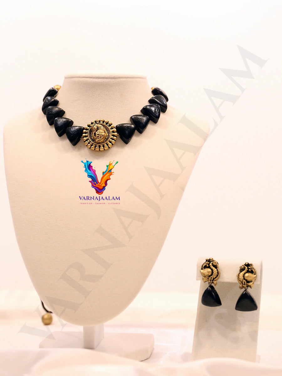 Terracotta choker with black triangular beads, a central antique gold peacock medallion, and matching peacock drop earrings
