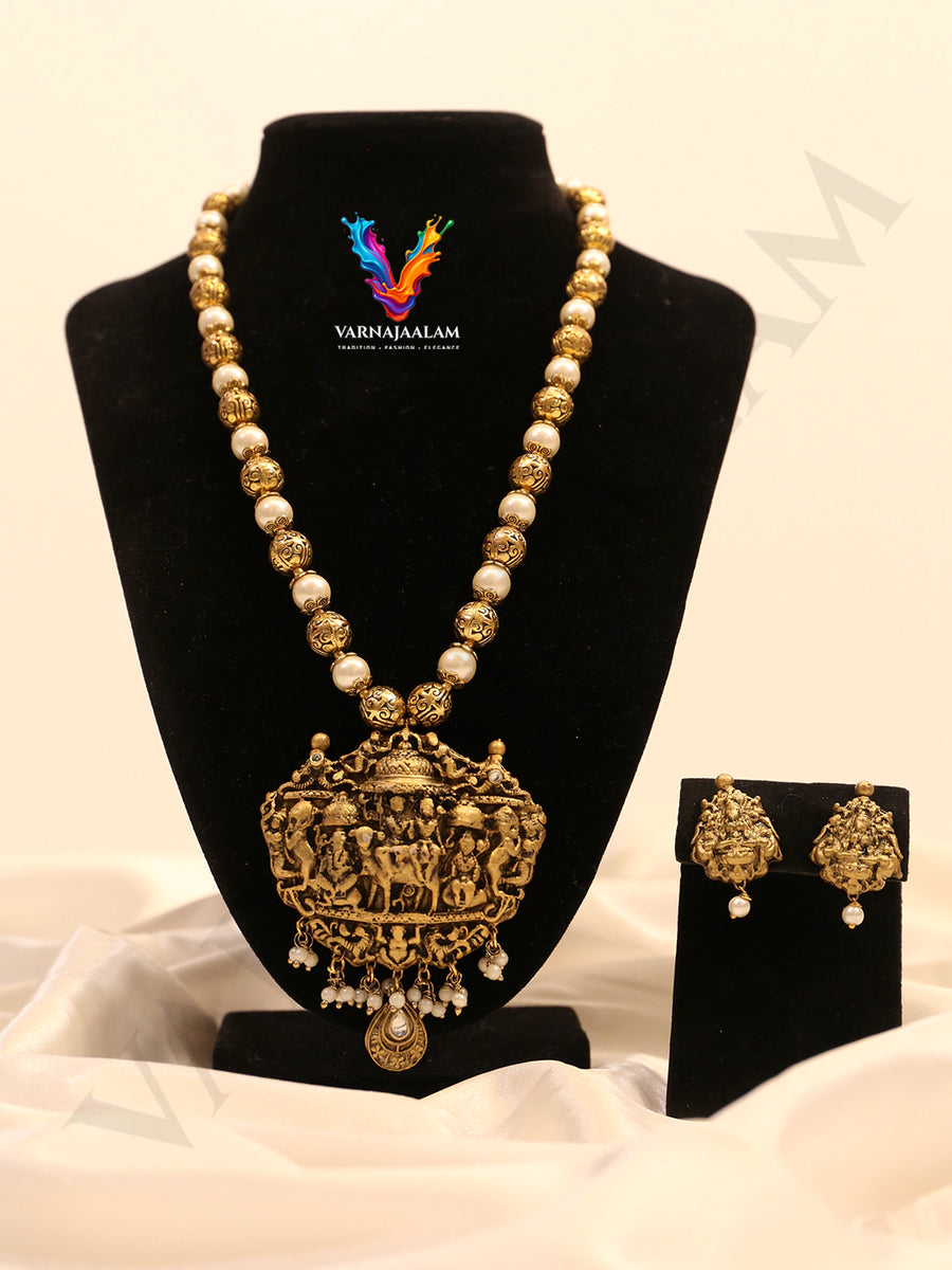 Handcrafted long mala featuring alternating white pearls, gold textured beads, and an ornate antique temple pendant