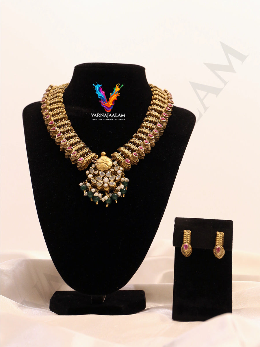 Terracotta antique gold structured choker lined with ruby stone studs, featuring a central floral Kundan pendant with green bead drops and matching post earrings
