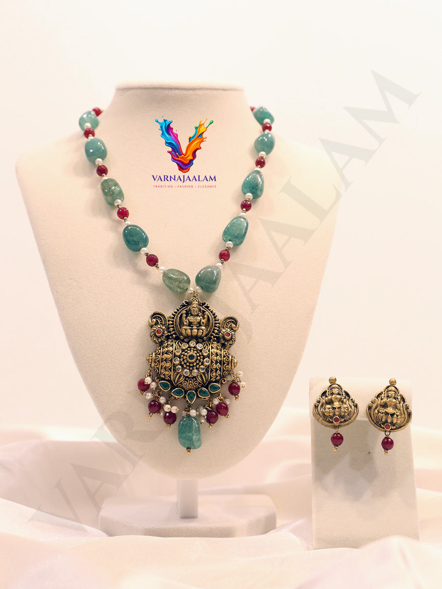 Terracotta long mala with green tumble beads and ruby red spacer beads, featuring an antique Lakshmi temple pendant with gemstone drops and matching Lakshmi earrings.